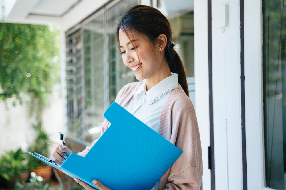 Private duty nurse jobs in the Bronx NY - smiling female RN reviewing patient care plan on clipboard outside home care location